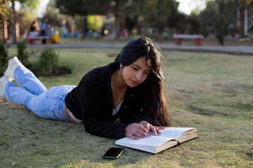 Young woman lying in a park reading a book. Concept of people and lifestyles.