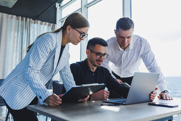 A team of businessmen in formal wear discussing project details and looking at laptop screen while collaborating during a meeting in a modern boardroom. Modern office