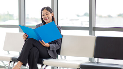 Millennial Asian happy cheerful successful professional female businesswoman employee in formal suit sitting smiling on chair take break holding document file folder in company office