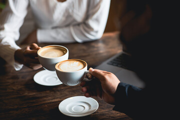 Close-up of a man and woman clinking a white coffee cup in a coffee shop. while talking at work