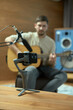 © Georgii - Musician playing acoustic guitar, records song on phone, shooting online lesson for social network. Guy out of focus