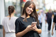 © Adam Radosavljevic - Beautiful smiling woman in black shirt texting on smartphone on street in city center