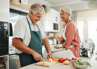Wall Mural - A happy senior couple, cooking healthy food in kitchen and drinking champaign as they enjoy retirement. Elderly woman with sitting on counter, man with silver laughing and they smile in love together