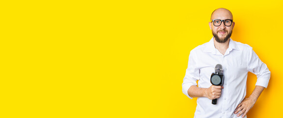 Smiling young man in glasses with a microphone on a yellow background. Banner