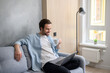 © Face Stock - Serene young 30s caucasian guy using laptop in relaxed home atmosphere, sitting on the sofa and typing, web surfing, watching movie. Carefree man drinking beverage