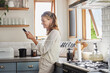 © Nina Lawrenson/peopleimages.com - Mature woman reading phone news, social media notification and mobile apps in Australia kitchen home. Happy lady typing smartphone, online social network and 5g web technology connection in apartment