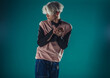 © qunica.com - Young adult man in casual outfit wear looking at camera, holding skateboard near face and standing at studio on blue background