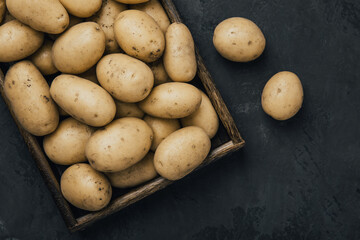 Wall Mural - Potato. Fresh raw organic potatoes in wooden box on dark stone background.