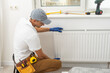 © Angelov - A male plumber installs a radiator in the heating system of an apartment. Guy in overalls and a gas wrench