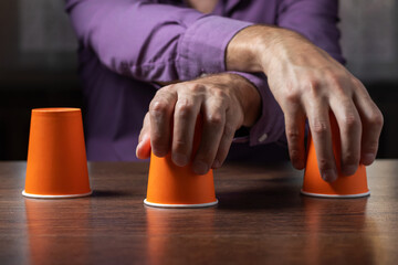 Wall Mural - Man shows shell game of thimbles with coin, dark background. Concept deception, sleight hand.