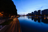 Fototapeta Las - View along the River Seine to the Eiffel tower, the river embankment, and the city at dusk, reflections on the water.