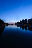 Fototapeta Las - View along the River Seine to the Eiffel tower, the river embankment, and the city at dusk, reflections on the water.