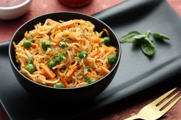 Schezwan Noodles or vegetable Hakka Noodles or chow mein, served in a bowl or plate with tomato sauce, ketchup, wooden chopsticks, India. popular Indo-Chinese Indian Maggi noodles.