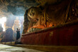 © Mint Images - A cave temple, a large reclining Buddha statue, lit candles and a monk praying.