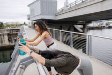 Female Joggers With Water Bottles Stretching At Bridge Railing