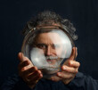 canvas print picture - a colorful man with curls, a beard and a silver-colored mustache holds a transparent glass ball in his hands and looks through this ball