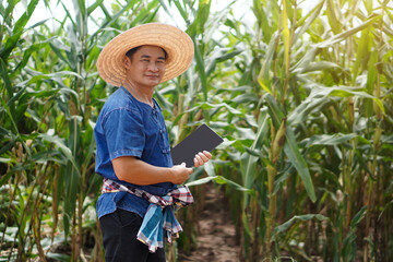 Wall Mural - Portrait of Asian man farmer wears hat, blue shirt and holds smart tablet at maize garden. Concept : smart farmer, use technology in agriculture. Happy farmer.          