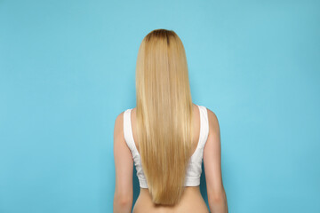 Canvas Print - Young woman with long straight hair on light blue background, back view