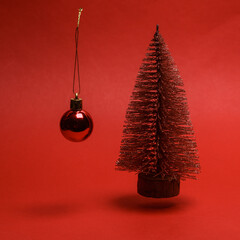 Wall Mural - Mini Christmas tree with a Christmas ball levitates on a red background