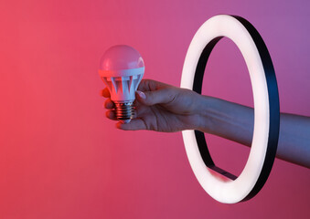 Wall Mural - Woman's hand holds led light bulb through led ring lamp in red blue neon gradient light. Creative idea.