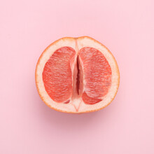 Gynecology, Female Intimate Hygiene. Half Of A Ripe Grapefruit Symbolizing The Female Vagina On A Pink Background. Creative Idea, Allegory, Fresh Idea. Top View