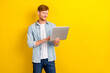 © deagreez - Photo portrait of charming young guy hold laptop coding test use new software wear stylish jeans outfit isolated on yellow color background