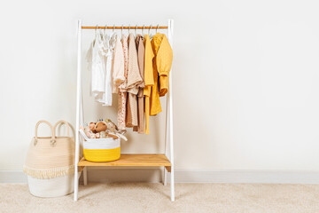 Clothing Rack with children's autumn outfit and Storage Baskets. Yellow, beige, white jacket, dress and sweaters on hangers in wardrobe. Nursery Storage Ideas. Home kids wardrobe.