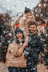 Winter holidays and people concept - happy family with little daughter choosing Xmas tree at Christmas tree fair. Happy preparation for the celebration of New Year holidays