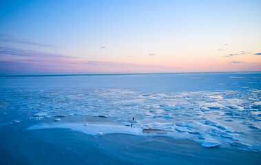 Aerial view - two people walk on ice on sunset over the frozen sea. Winter landscape on seashore during dusk. View from above of melting ice in ocean on sunrise. Global warming. Vivid colorful skyline