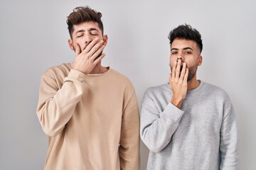 Wall Mural - Young homosexual couple standing over white background bored yawning tired covering mouth with hand. restless and sleepiness.