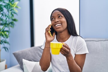 Wall Mural - Young african american woman talking on the smartphone drinking coffee at home