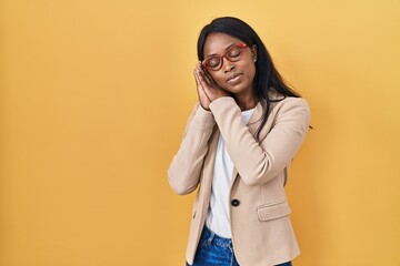 Wall Mural - African young woman wearing glasses sleeping tired dreaming and posing with hands together while smiling with closed eyes.