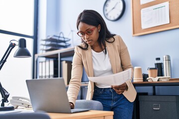 Wall Mural - Young african american woman business worker using laptop holding paperwork at office