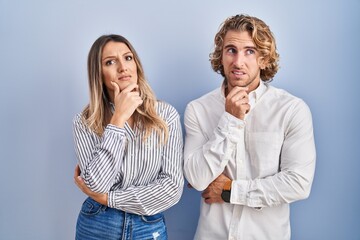 Wall Mural - Young couple standing over blue background thinking worried about a question, concerned and nervous with hand on chin