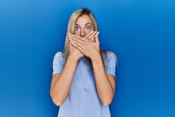 Wall Mural - Beautiful blonde woman wearing casual t shirt over blue background shocked covering mouth with hands for mistake. secret concept.