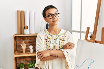 Wall Mural - Young hispanic woman with short hair at art studio smiling looking to the side and staring away thinking.