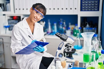 Canvas Print - Young beautiful hispanic woman scientist smiling confident writing on document at laboratory