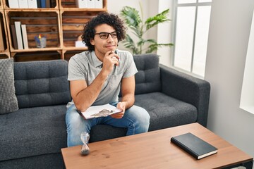 Wall Mural - Young hispanic man psychologist writing on clipboard at psychology center