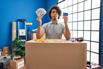 Poster - Hispanic man with curly hair moving to a new home holding money and credit card making fish face with mouth and squinting eyes, crazy and comical.