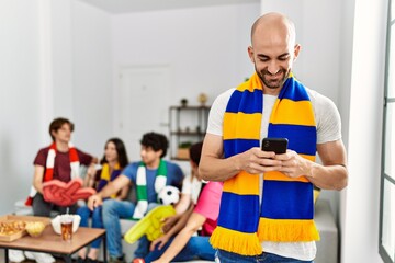 Poster - Group of young hispanic friends watching and supporting soccer match. Man smiling happy and using smartphone at home.