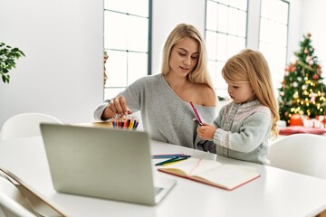 Wall Mural - Mother and daughter drawing on notebook using laptop sitting by christmas tree at home