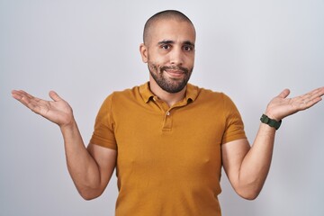 Sticker - Hispanic man with beard standing over white background clueless and confused expression with arms and hands raised. doubt concept.