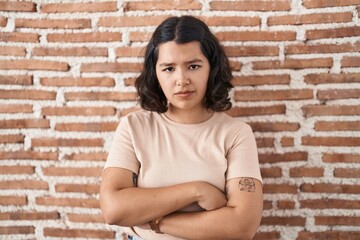 Sticker - Young hispanic woman standing over bricks wall skeptic and nervous, disapproving expression on face with crossed arms. negative person.