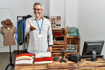 Poster - Middle age hispanic man working as manager at retail boutique smiling cheerful offering palm hand giving assistance and acceptance.