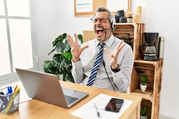 Sticker - Middle age hispanic business man working at the office wearing operator headset celebrating mad and crazy for success with arms raised and closed eyes screaming excited. winner concept