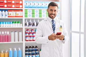 Poster - Young hispanic man pharmacist using smartphone working at pharmacy