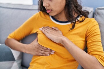 Poster - Young african american woman examining breast sitting on sofa at home