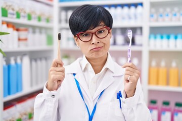 Sticker - Young asian woman with short hair doing toothbrush comparative at pharmacy skeptic and nervous, frowning upset because of problem. negative person.