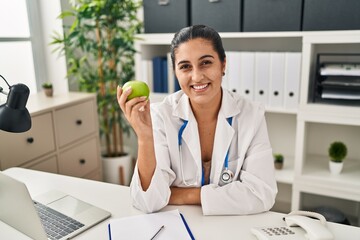Poster - Young hispanic woman wearing dietitian uniform holding apple at clinic