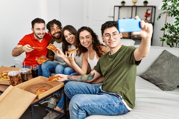 Wall Mural - Group of young friends smiling happy eating italian pizza make selfie by the smartphone at home.